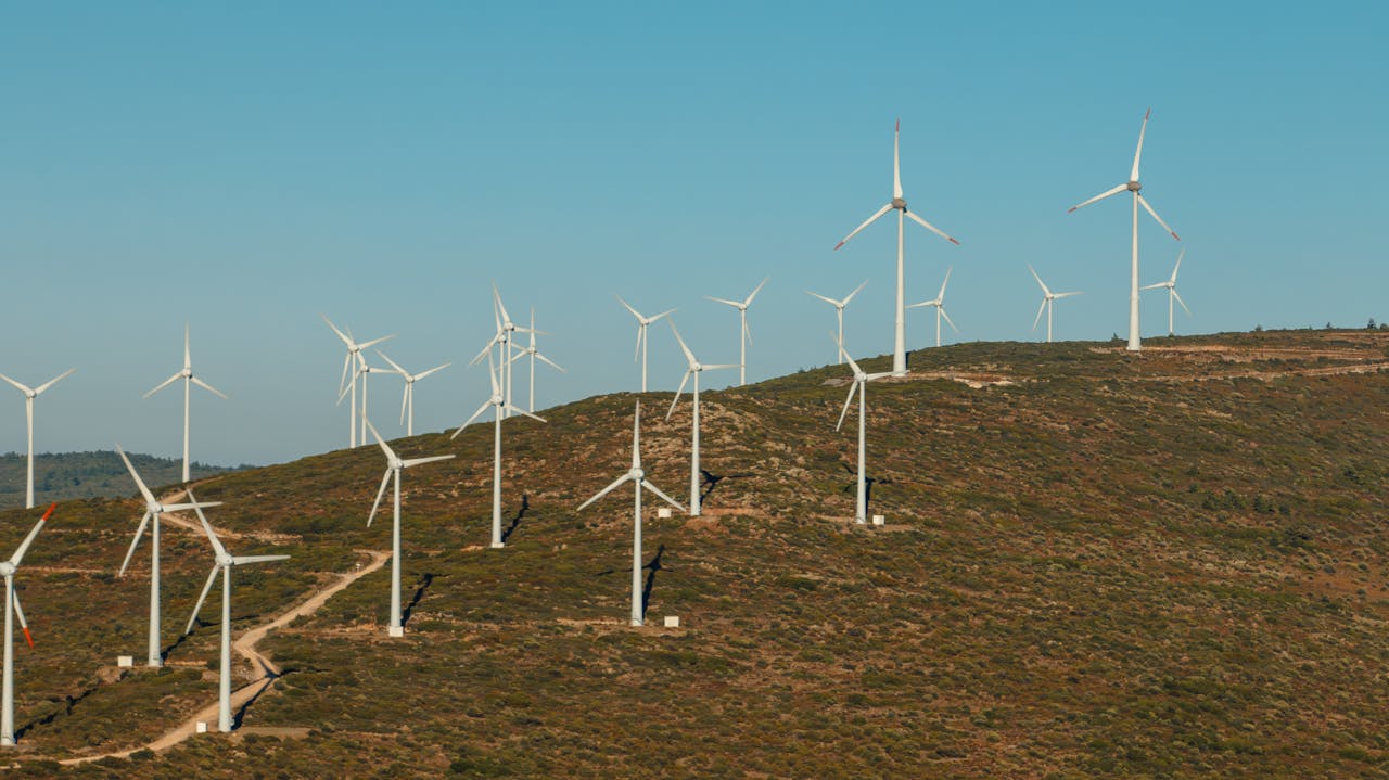 Vue panoramique d'un parc éolien utility-scale installé sur des collines au coucher du soleil, montrant plusieurs rangées de turbines éoliennes blanches raccordées au réseau électrique.